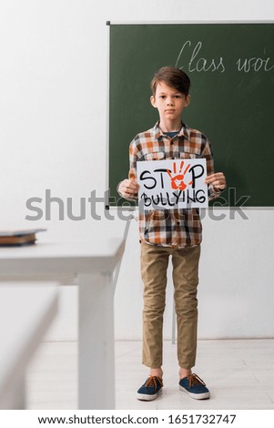 selective focus of schoolboy holding placard with stop bullying lettering