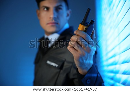 Professional security guard with portable radio set near window in dark room, focus on hand