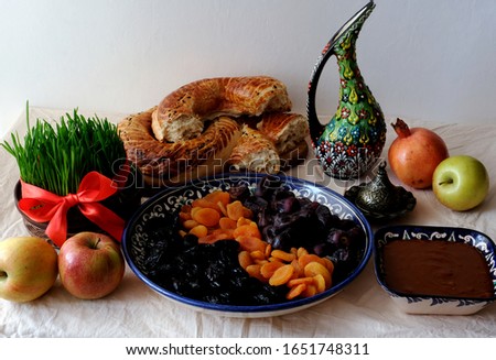 Traditional food of holiday Navruz: national dessert of Central Asia called Sumalak, lavash bread, assortment of dry fruits and fresh fruits. Young green wheat with red ribbon.