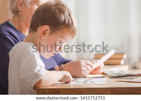 little boy 4 years old reading book. He is sitting on chair  in sunny living room watching pictures in story. Kid doing homework for elementary school or kindergarten. Children study.