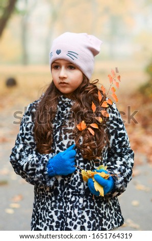 
5 years old girl. on the head a pink hat, against the background of an orange bush