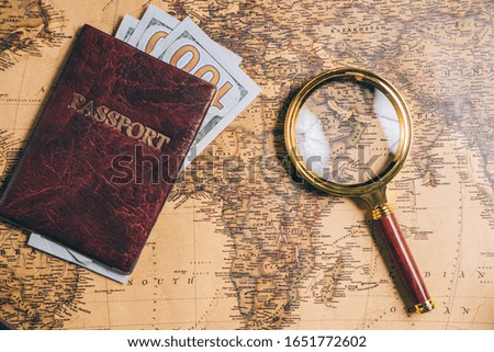 Magnifying glass and passport with money on a vintage world map. View from above.