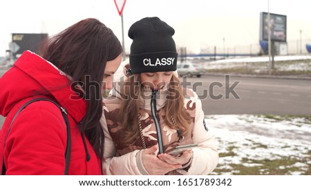 The meeting of girlfriends on street. Two women look in mobile phone, considering their photos on walk.