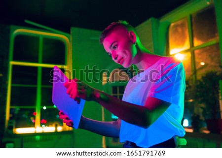 Gaming. Cinematic portrait of stylish woman in neon lighted interior. Toned like cinema effects, bright neoned colors. Caucasian model using tablet in colorful lights indoors. Youth culture.