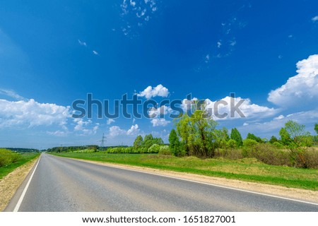 spring photo taken with a wide-angle lens, local highway, bright green trees, clouds in the blue sky