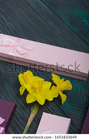 A bouquet of yellow daffodils lies on the surface of brushed pine boards. Near cardboard boxes with gifts. Pink and lilac, decorated with ribbon bows.