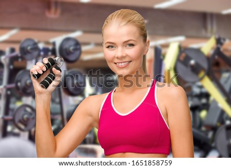 sport, fitness and people concept - beautiful happy smiling woman with hand expander exercising over gym on background