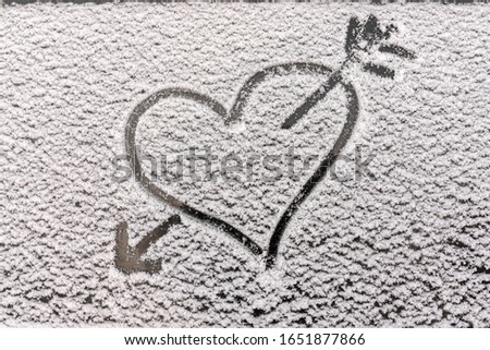 a heart and an arrow from a bow piercing it, a close-up silhouette on the snow, drawn on the glass with a finger. Romantic picture, love separation and parting and other emotions. copyspace