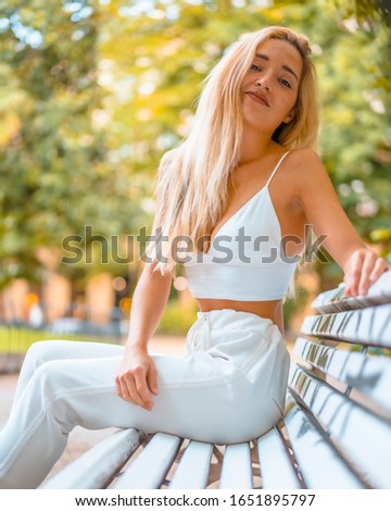 Street style, young blonde smiling caucasian girl sitting on a white chair in the city