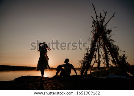 Young couple is embracing in the water on Sunset. Two silhouettes against the sun. Romantic love story. Wigwam on the stone.