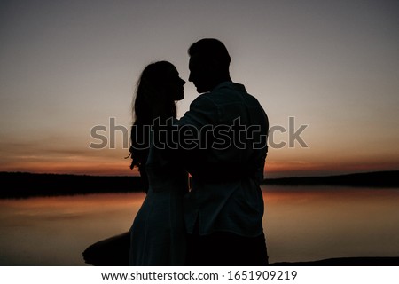 Young couple is embracing on the sunset coast. Two silhouettes against the sun. Romantic love story.