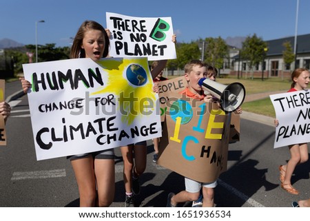 Front view close up of a group of Caucasian elementary school pupils on a protest march, carrying signs with environmental and conservation slogans on them, and one boy shouting in a megaphone while