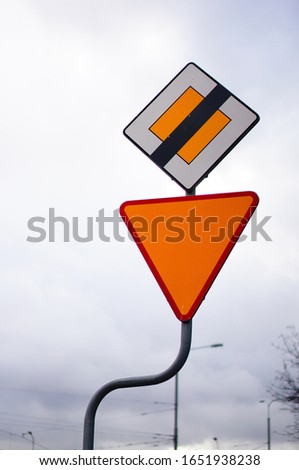 A vertical picture of road signs under a cloudy sky with a blurry background