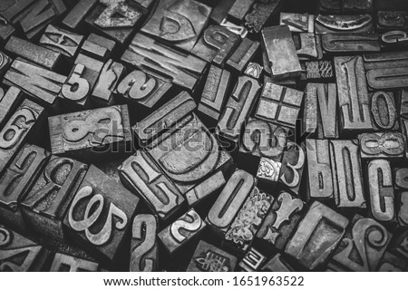 A black and white textured background of a heap of antique wooden type-setting letter blocks with various fonts, upper- and lowercase, antique letters used for printing books and newspapers. 
