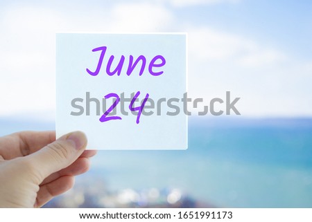 June 24th. Hand holding sticker with text June 24 on the blurred background of the sea and sky. Copy space for text. Month in calendar concept