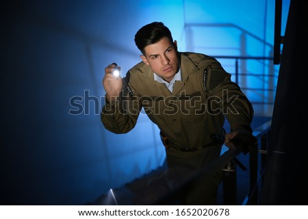 Professional security guard with flashlight on stairs in dark room