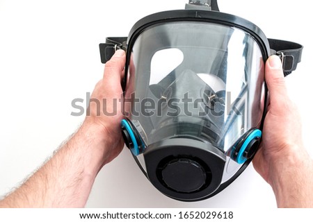 a gas mask with panoramic glass is held in both hands on a white background. concept of protection against virus and other harmful factors