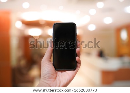Mock up image of man hand touching smartphone with black screen hand blurred modern office background, home interior, living room, copy space.