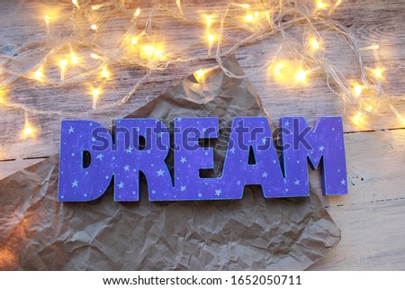 Wooden word DREAM of lilac color with stars and space. Light background with lights, bokeh.