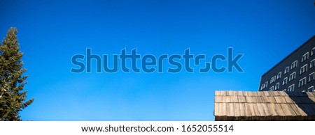 A wooden small roof and behind it is a beautiful clear blue sky. There is a sunny day on the mountain.