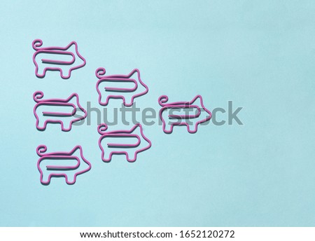 top view of group with pink piggy paper clips in one direction with leader in front on blue background,  leadership concept