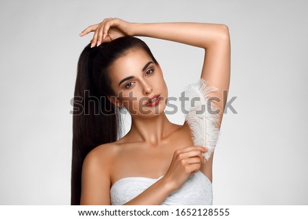 Armpit epilation, hair removal. Young woman holding her arms up and showing clean underarms, depilation smooth clear skin . Beauty portrait. armpit's care. Large white feather near skin Royalty-Free Stock Photo #1652128555