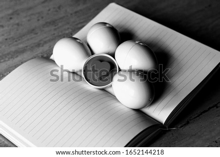 Half an egg with an embossed heart pattern lying next to other eggs on an orange notebook(black and white picture).