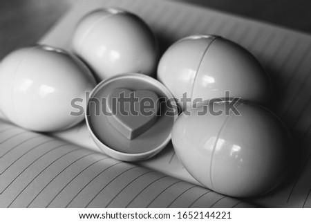 Half an egg with an embossed heart pattern lying next to other eggs on an orange notebook(black and white picture).