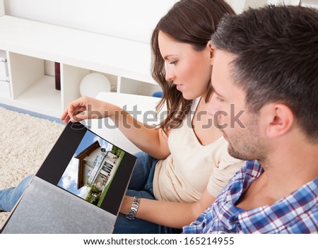 Young Couple Sitting On Couch Looking At Picture Of Real Estate