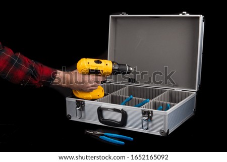 a worker in a red plaid shirt removes an electric drill from an aluminum case isolated on black