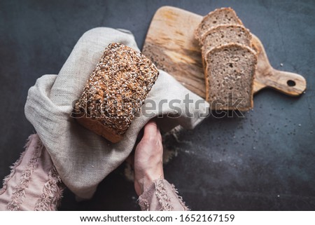 Woman's hands holding a loaf of buckwheat bread with chia. Top view.