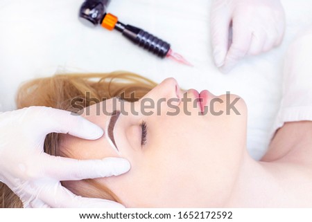 Make-Up. Beautician Hands Doing Eyebrow Tattoo On Woman Face.Permanent Brow Makeup In Beauty Salon. Vertical photo. Cosmetology Treatment.