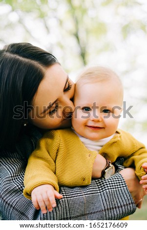 a young mother holds a small happy son in her arms near a small stream in an autumn Park