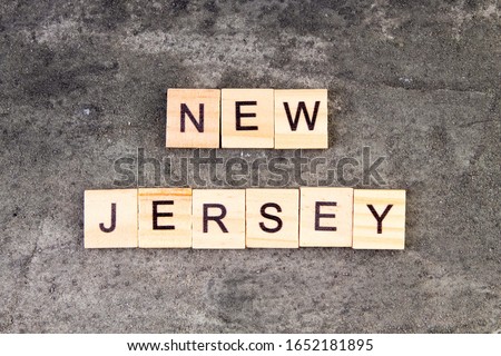 New Jersey word written on wood block, on gray concrete background. Top view