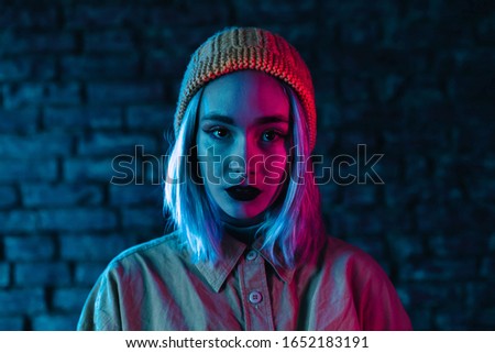 Young woman in pink and blue neon light. Portrait of unusual beautiful punk girl with colorful hairstyle on bricks wall studio background Royalty-Free Stock Photo #1652183191