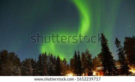 View of green northern lights with some cottages and trees