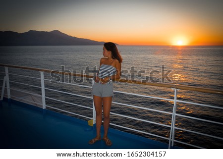 Asian teen in tube top standing on deck of ferry looking away from sunset on ferry to Greece