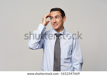 A man in a shirt and tie scratches his head with his hand
