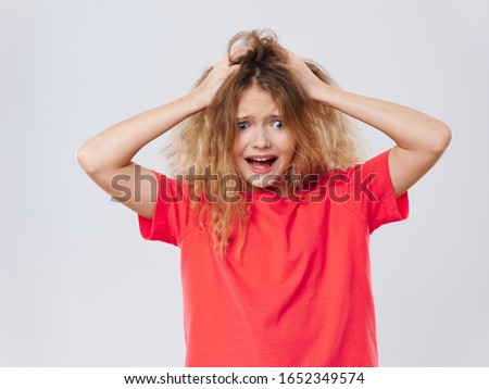 A girl in a red shirt touches the hair on her head