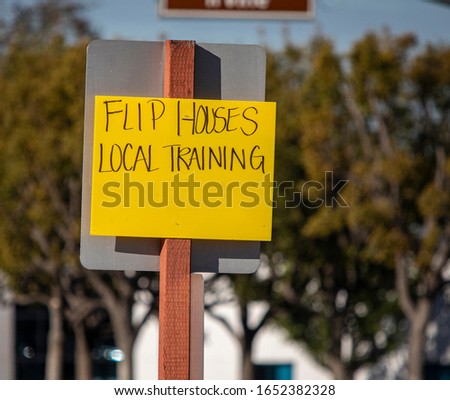 Yellow handwritten sign recruiting for get rich quick by flipping houses at intersection