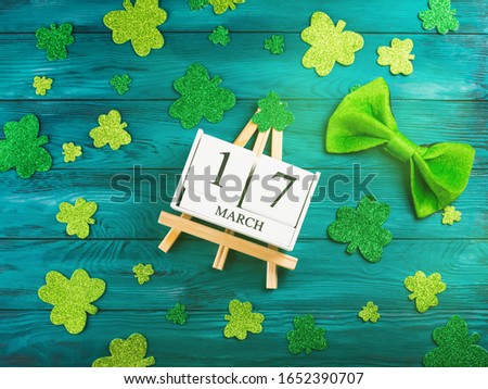St Patricks Day date 17 march on wooden calendar on dark green wooden rustic background with shamrocks around and leprechaun costume accessory