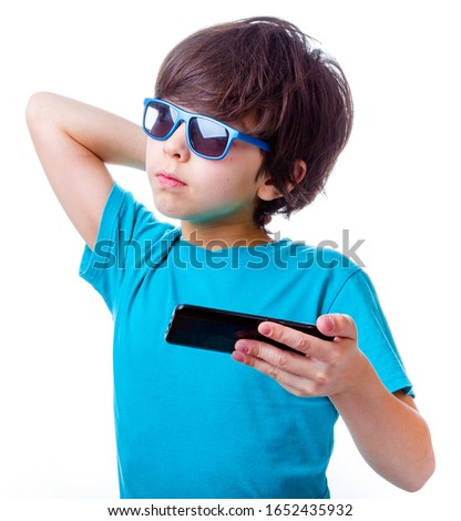 Emotional little boy playing with smartphone, in blue clothes and sunglasses, thought looking up, on white background
