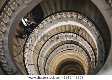Shallow depth of field (selective focus) image with a woman journalist using her laptop and mobile phone on a very deep spiral staircase