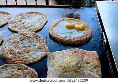 A picture of "roti sarang" in the making at the hot pans. It is pratha looks like bird nest with half cook eggs in the middle.