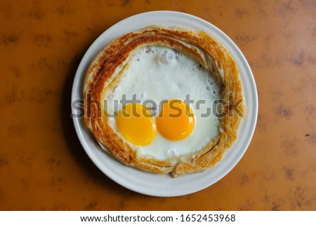 Flatlay picture of "roti sarang burung" on the table. It is pratha looks like bird nest with half cook eggs in the middle.