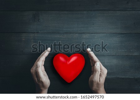 Man Hands protect red heart on wood table background. Save health , family or love  concept.
