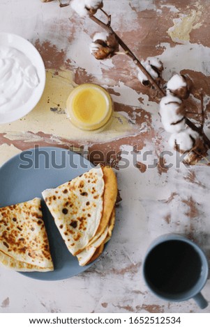 Cute pancake day breakfast. Stack of delicious homemade pancakes on plate with honey, sour cream and tea.  Maslenitsa Butter Week festival meal. Rustic style, close up, top view. Flat lay