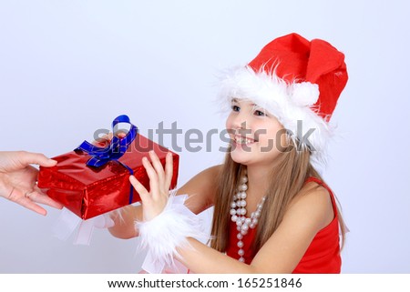 A portrait of a cute beautiful young girl with long hair in a red dress and santa hat getting a christmas present