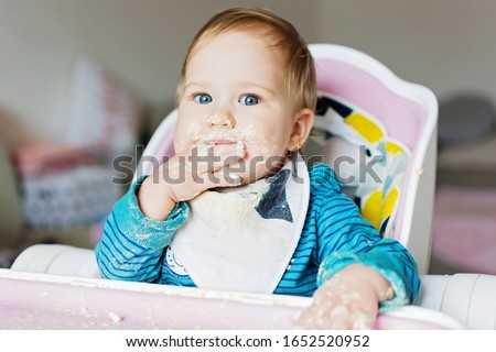 Cute baby self-feeding with messy face and hands. Adorable baby eating by herself make mess with food Royalty-Free Stock Photo #1652520952