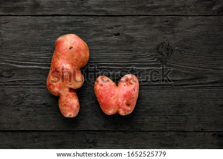 Ugly funny vegetables, heart-shaped potatoes and letter shape on a black wooden background. The concept of grungy vegetables or food waste. Top view, copy space.